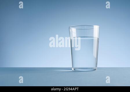 Minimalistisches Foto eines Glases sauberen Trinkwassers auf blauem Hintergrund Stockfoto