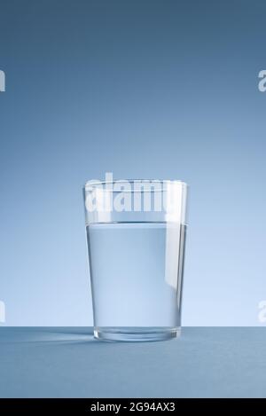 Minimalistisches Foto eines Glases sauberen Trinkwassers auf blauem Hintergrund Stockfoto
