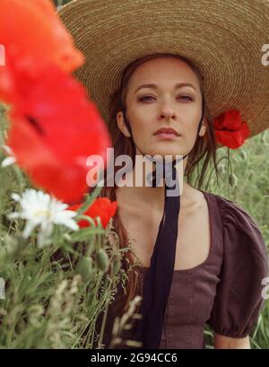 Nahaufnahme Porträt einer Frau mit Hut sitzt zwischen Mohnblumen Blume Stockfoto