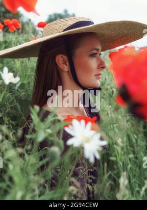 Nahaufnahme Porträt einer Frau mit Hut sitzt zwischen Mohnblumen Blume Stockfoto