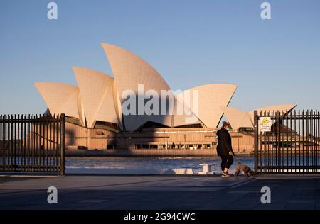 Sydney, Australien. Juli 2021. Eine Frau geht mit einem Hund in der Nähe des Sydney Opera House in Sydney, Australien, 24. Juli 2021. Da der Pandemieausbruch im australischen Bundesstaat New South Wales (NSW) weiter ansteigt, erklärten die staatlichen Behörden den Ausbruch am Freitag zu einem nationalen Notfall und forderten die Umleitung der nationalen Impfstofflieferungen. Quelle: Bai Xuefei/Xinhua/Alamy Live News Stockfoto