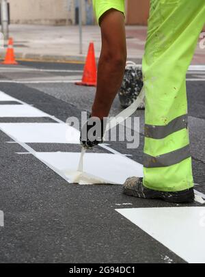 Arbeiter in reflektierenden Hosen entfernt thermoplastisches Markierungsband von Straßenarbeiten, um Verkehrslinien und Fahrradwege auf Asphalt zu lackieren, selektiv Stockfoto