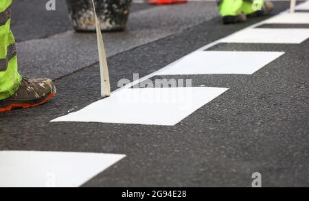 Lackierung der Verkehrslinie. Die Arbeiter malen weiße Linien auf dem Fußgängerüberweg. Straßenkegel mit orangefarbenen und weißen Streifen im Hintergrund, auf Asphalt d Stockfoto