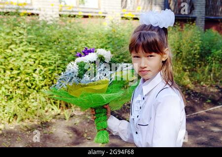 Ein Mädchen mit einem Blumenstrauß und einer Aktentasche geht am 1. September Stockfoto