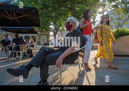 Mann mit einer Maske, der sich von Menschen entfernt, die in der Nähe von King's Rd, London, Großbritannien, sitzen Stockfoto