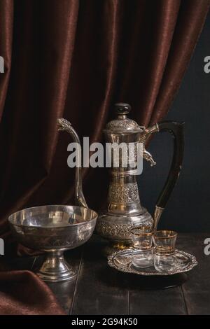 Stillleben mit antikem ostmetallischem Geschirr - Vintage-Krug für Wasser oder Tee, eine Vase für Obst und ein Teller mit orientalischer Dekoration. Stockfoto