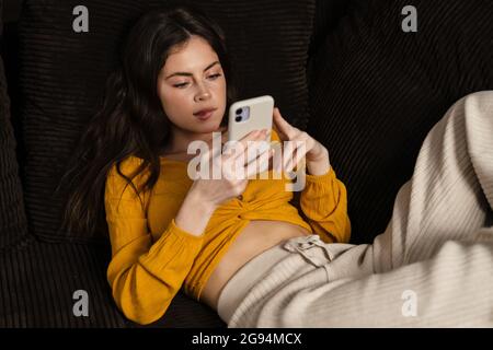Junge Brünette Frau mit Mobiltelefon, während sie auf einer Couch lag Stockfoto