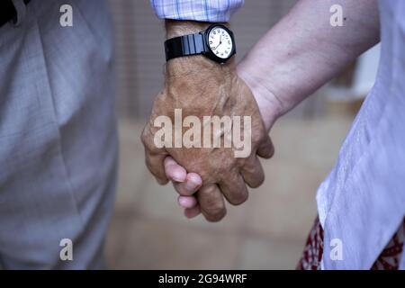 Ein älteres Paar hält sich die Hände, du und ich für immer. Nahaufnahme eines älteren Ehepaares, das sich in einem Gebäude die Hände hält, und er trägt eine Armbanduhr Stockfoto