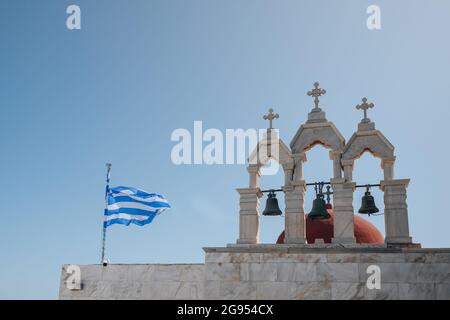 Ana Mera, Griechenland - 24. September 2019: Griechische Flagge und Glocken auf dem Panagia Tourliani-Kloster, einer weiß getünchten Kirche und einem Kloster auf Mykonos Stockfoto