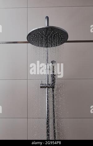 Dusche mit gefliestem Hintergrund im Badezimmer. Wasser fliegt in Tropfen aus Chrom-Duschen. Badausstattung als Ausstattungselement und modernes Design zu Hause. Stockfoto