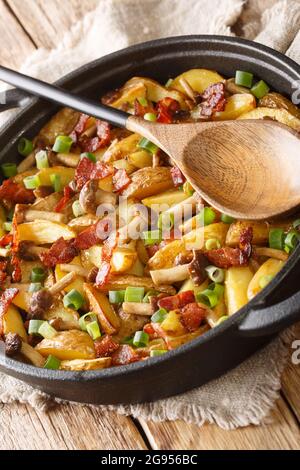 Gebratene Kartoffeln mit Speck und Pilzen in einer Pfanne auf dem Tisch aus nächster Nähe. Vertikal Stockfoto