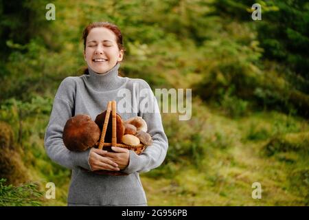 Eine Frau mit einem Korb voller verschiedener Pilze im Wald Stockfoto