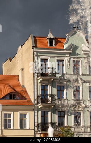 Abendliches Sonnenlicht an den Fassaden - Altstadt in Gniezno, Polen. Brunnenschub, Wassertropfen, Hauptstraße in der Stadt als Hintergrund. Stockfoto