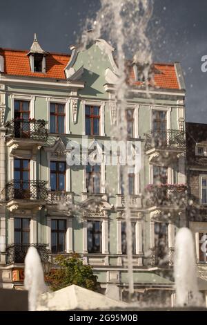 Abendliches Sonnenlicht an den Fassaden - Altstadt in Gniezno, Polen. Brunnenschub, Wassertropfen, Hauptstraße in der Stadt als Hintergrund. Stockfoto