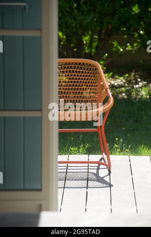 Rattansessel auf einer Holzterrasse vor einem französischen Fenster im Sommer Stockfoto