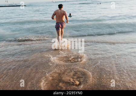 Erwachsener Mann läuft und spritzt in den Ozean am Waikiki Strand Stockfoto