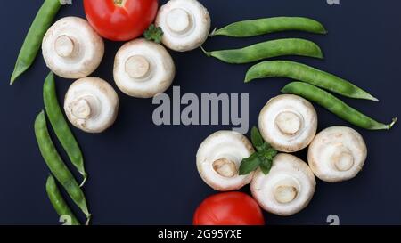 Pilze, Tomaten, Minze und grüne Erbsen auf dunklem Grund Stockfoto