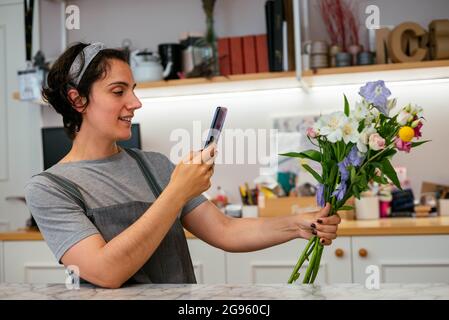 Junge Floristin, die in ihrem Atelier Blumen fotografiert Stockfoto