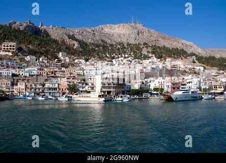 Pothia, der Hafen der griechischen Insel Kaymnos. Steile Hänge erheben sich über der Uferpromenade und blicken auf die Bucht darunter. Ein geschäftiger, geschäftiger Hafen Stockfoto