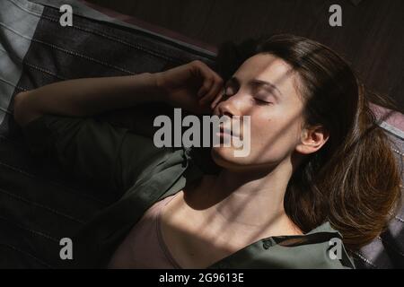 Porträt einer jungen Frau, die in sonnigen Strahlen im Bett schläft Stockfoto