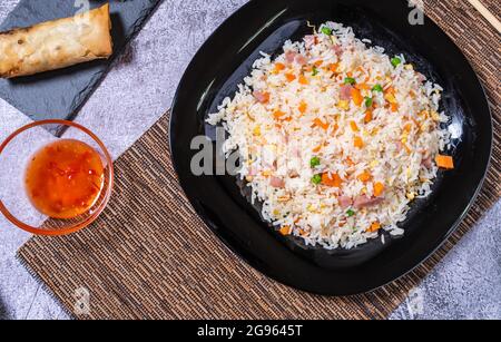 Blick von oben auf chinesisches Essen. Schwarzer Reisplatte 3 Köstlichkeiten, Schüssel mit süß-saurer Sauce und Frühlingsrollen. Asiatische Küche Stockfoto