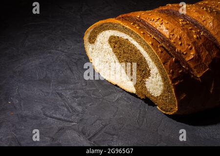 Ungewöhnlicher zweifarbiger frischer Laib Brot auf schwarzem Hintergrund, Foto in einer niedrigen Taste bei hartem Licht, Nahaufnahme Stockfoto