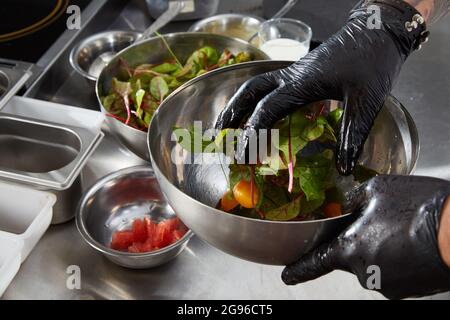 Nahaufnahme der Hände des Küchenchefs, die Salat in einer Restaurantküche zubereiten Stockfoto