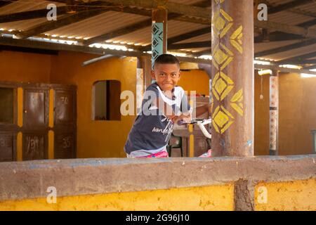 Uribia, La Guajira, Kolumbien - 28 2021. Mai: Wayuu Boy fährt Fahrrad und schaut an einem sonnigen Tag auf die Kamera Stockfoto