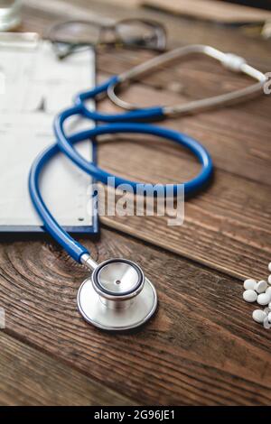 Nahaufnahme der Krankenkarte des Patienten, Stethoskop und Pillen auf dem Arzttisch Stockfoto