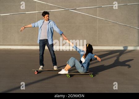 Aktive Paare reiten gerne gemeinsam auf Longboard auf der sommerlichen Stadtstraße. Mann lehrt Frau Skateboarding Stockfoto