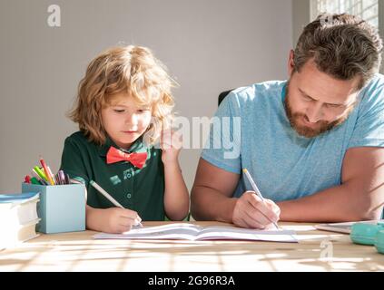 Bärtiger Vater schreibt Schulaufgaben mit seinem Sohn im Klassenzimmer, Bildung Stockfoto