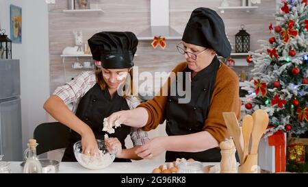 Enkelin mit Oma bereitet traditionelle hausgemachte Teigbacken traditionelle Kekse Dessert in der kulinarischen Küche während der weihnachtszeit. Familie feiert weihnachtsferien und genießt das Kochen Stockfoto
