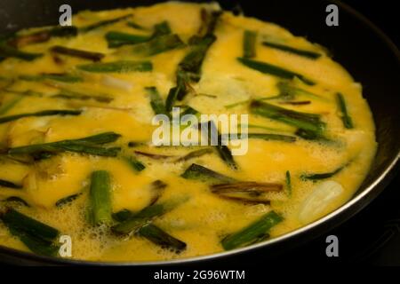 Nahaufnahme eines gehackten Knoblauchomeletts mit dem Ei ohne Gerinnung in einer Bratpfanne auf einem schwarzen Glaskeramikkochfeld Stockfoto