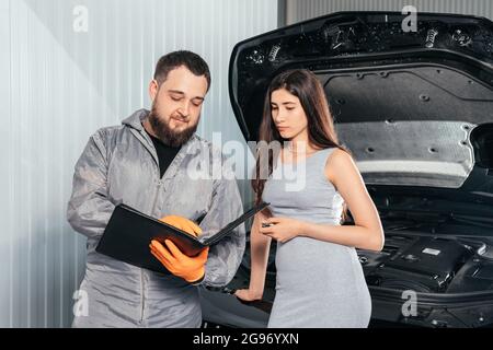 Auto Mechanic erklärt weiblichen Kunden die Fahrzeugreparaturrechnung und unterschreibt Papiere Stockfoto