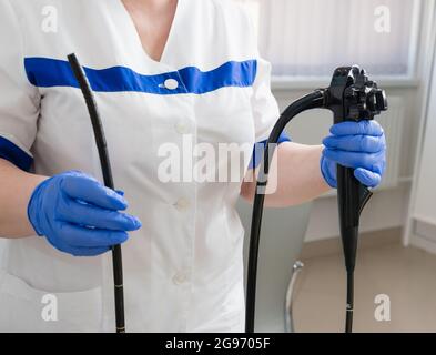 Eine Ärztin im weißen Anzug hält medizinische Geräte für die Video-Ösophagododenoskopie in ihren Händen in blauen Handschuhen. Endoskopie-Raum Stockfoto