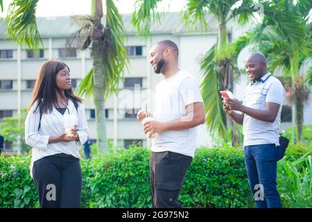 Afrikanische Freunde, bestehend aus einem Mann und einer Dame, die zusammen mit ihrem Freund in einem wunderschönen Outdoor-Park am Telefon chatten Stockfoto