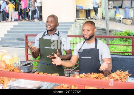 Zwei männliche afrikanische Barbeque- und Hühnerverkäufer lächeln und begrüßen Kunden, um ihr Geschäft zu bevormunden Stockfoto