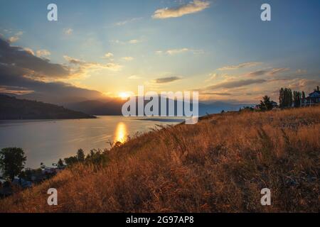 Der Blick vom Hang auf den Sonnenaufgang über den Bergen und dem Fluss und spiegelte sich im Wasser wider. Stockfoto