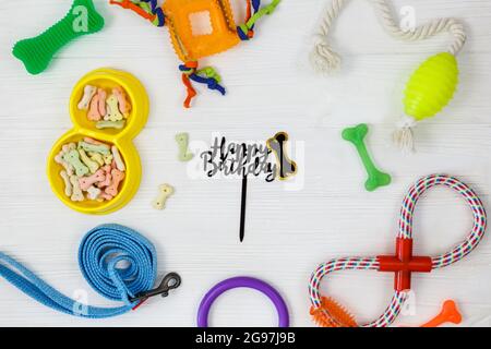 Gelbe Schale mit Snacks, Ball, Leine, ein Knochenspielzeug für Hunde auf weißem Holztisch. Set von Zubehör für Haustiere auf Holz. Nahaufnahme Stockfoto