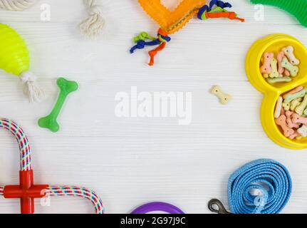 Gelbe Schale mit Snacks, Ball, Leine, ein Knochenspielzeug für Hunde auf weißem Holztisch. Set von Zubehör für Haustiere auf Holz. Nahaufnahme Stockfoto