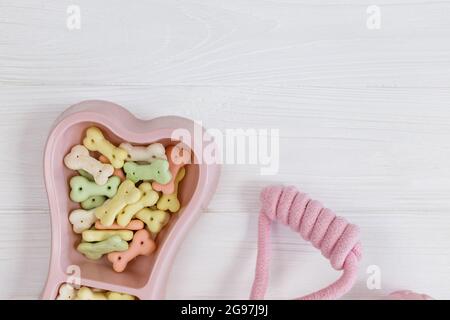 Rosa Schale mit Snacks, Ball, Leine, ein Knochenspielzeug für Hunde auf einem weißen Holztisch. Set von Zubehör für Haustiere auf Holz. Nahaufnahme Stockfoto