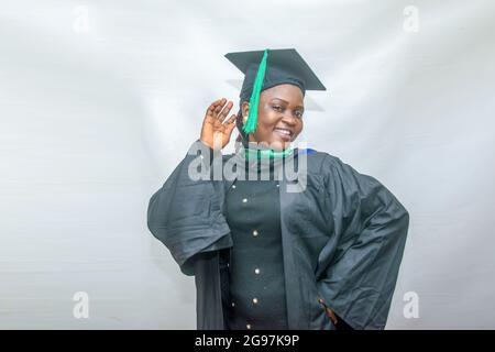 Stock-Foto einer afrikanischen Graduiertenin oder graduierenden Studenten, die ihren Körper freudig in ihrem schwarzen Graduierungsoutfit bewegen Stockfoto