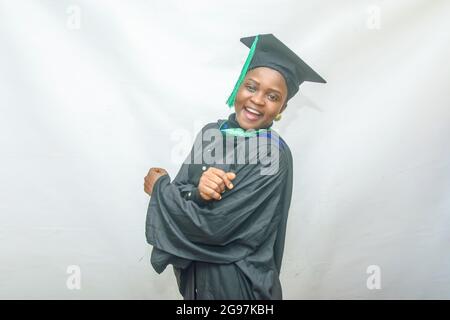 Stock-Foto einer afrikanischen Graduiertenin oder graduierenden Studenten, die ihren Körper freudig in ihrem schwarzen Graduierungsoutfit bewegen Stockfoto