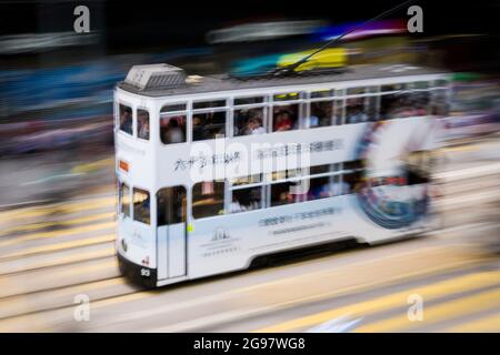 Eine Straßenbahn fährt entlang der des Voeux Road, Central, Hong Kong Island, in einer Schwenkaufnahme mit selektiven Bewegungsunschärfen aufgrund von Kamerabewegungen Stockfoto