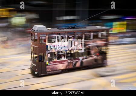 Eine Straßenbahn fährt entlang der des Voeux Road, Central, Hong Kong Island, in einer Schwenkaufnahme mit selektiven Bewegungsunschärfen aufgrund von Kamerabewegungen Stockfoto