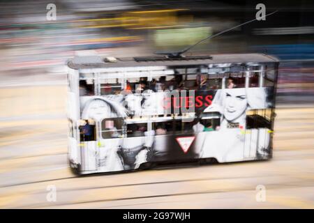 Eine Straßenbahn fährt entlang der des Voeux Road, Central, Hong Kong Island, in einer Schwenkaufnahme mit selektiven Bewegungsunschärfen aufgrund von Kamerabewegungen Stockfoto