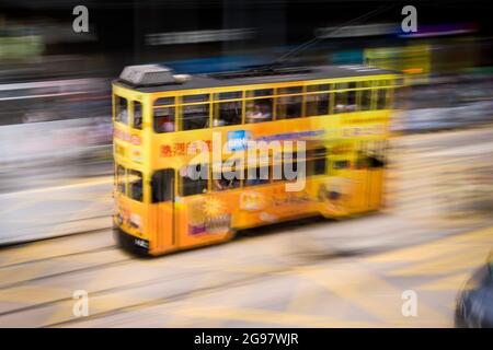 Eine Straßenbahn fährt entlang der des Voeux Road, Central, Hong Kong Island, in einer Schwenkaufnahme mit selektiven Bewegungsunschärfen aufgrund von Kamerabewegungen Stockfoto