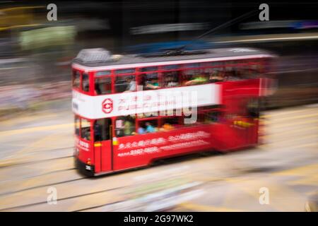 Eine Straßenbahn fährt entlang der des Voeux Road, Central, Hong Kong Island, in einer Schwenkaufnahme mit selektiven Bewegungsunschärfen aufgrund von Kamerabewegungen Stockfoto