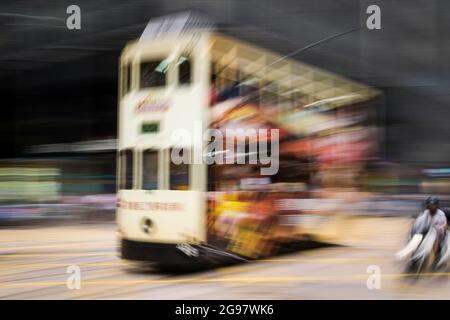 Eine Straßenbahn fährt entlang der des Voeux Road, Central, Hong Kong Island, in einer Schwenkaufnahme mit selektiven Bewegungsunschärfen aufgrund von Kamerabewegungen Stockfoto