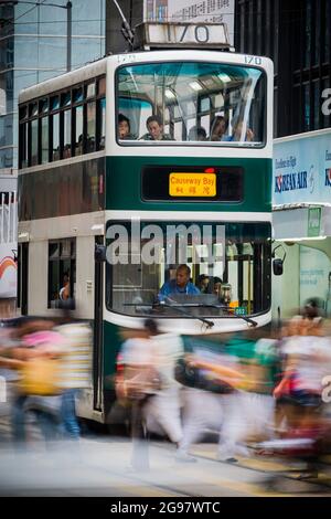 Fußgänger überqueren die des Voeux Road, Central, Hong Kong Island, vor einer der drei Millennium-Straßenbahnen in der Flotte, die an einer roten Ampel warten Stockfoto